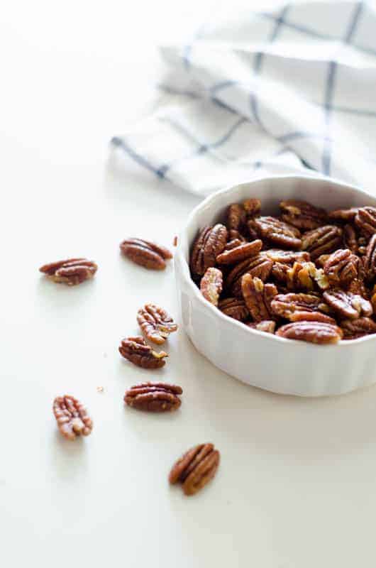 Bowl of pecans with white and blue dishtowel in the background and pecans scattered nearby