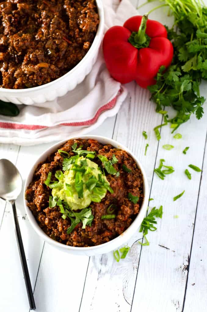 Overhead view of bowl of paleo chili surrounded by fresh peppers and herbs