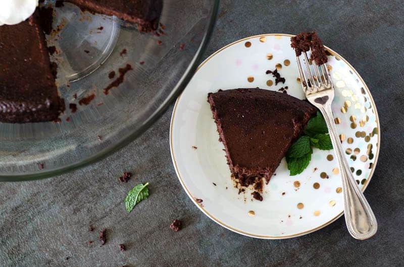 overhead view of a slice of paleo flourless chocolate cake on a plate with a fork taken from a nearby cake 