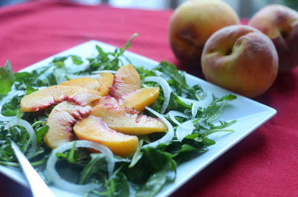 side view of a salad of peaches and onions on top of arugula with peaches in the background