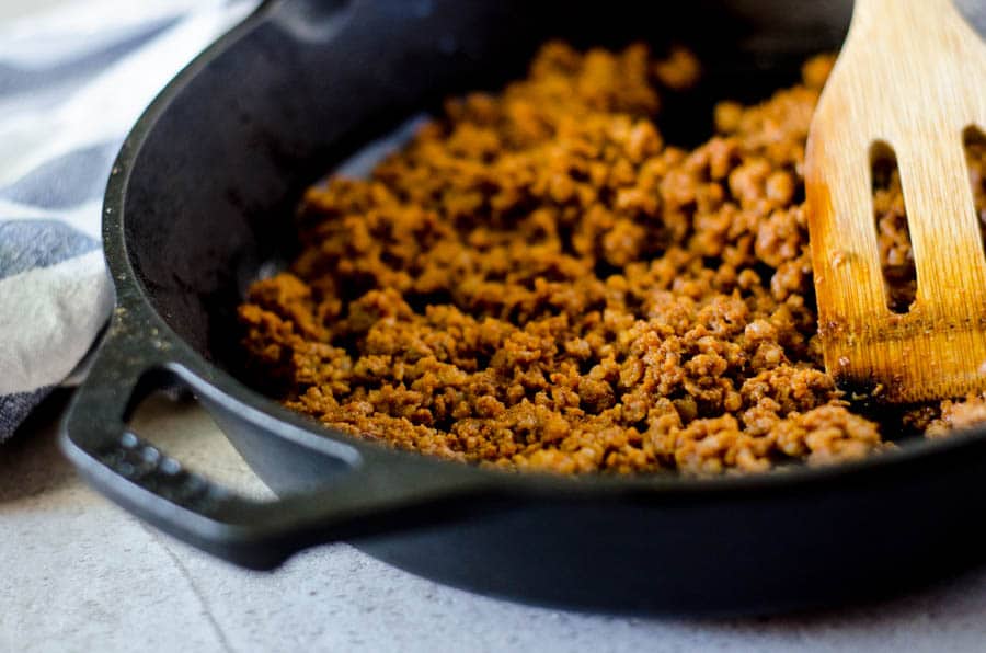 Side view of a cast iron skillet with chorizo sausage in it with a wooden utensil