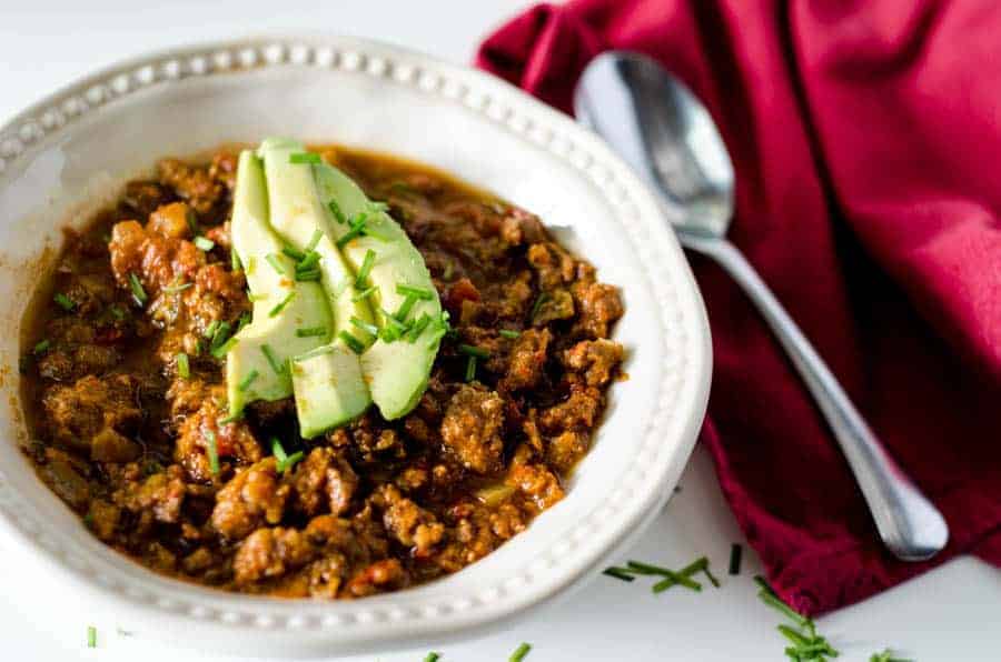 white bowl full of Instant Pot pumpkin chili topped with avocado slices with red napkin and spoon next to it