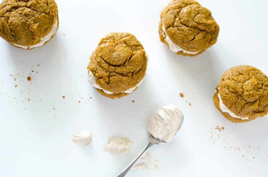 overhead view of 4 pumpkin whoopie pies surrounded by cinnamon and dollops of cream filling 