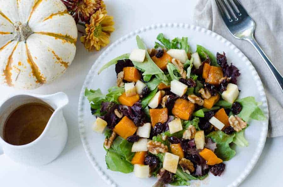 overhead view of plated fall salad with salad dressing and a decorative pumpkin in the background