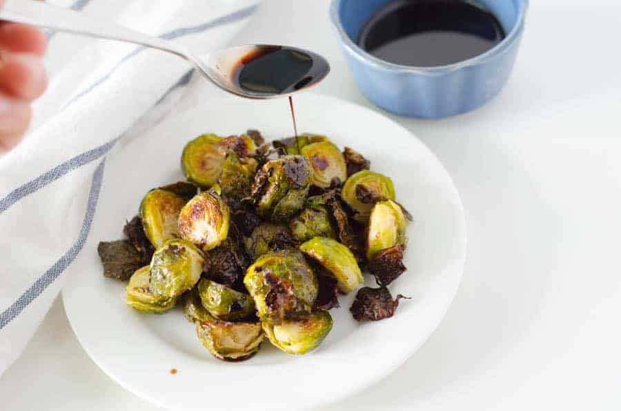 brussel sprouts on a plate being drizzled with balsamic glaze from a spoon