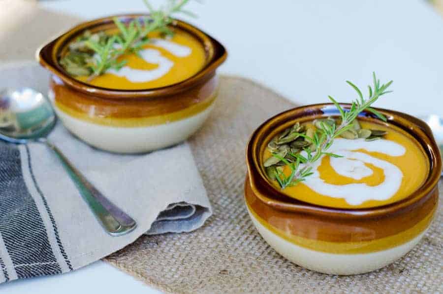 curried sweet potato soup in 2 bowls with sprigs of rosemary on top