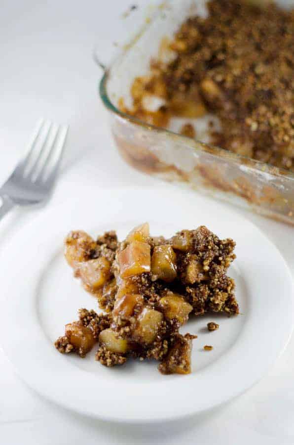 close up of a serving of paleo apple crisp on a white plate with serving dish in the background