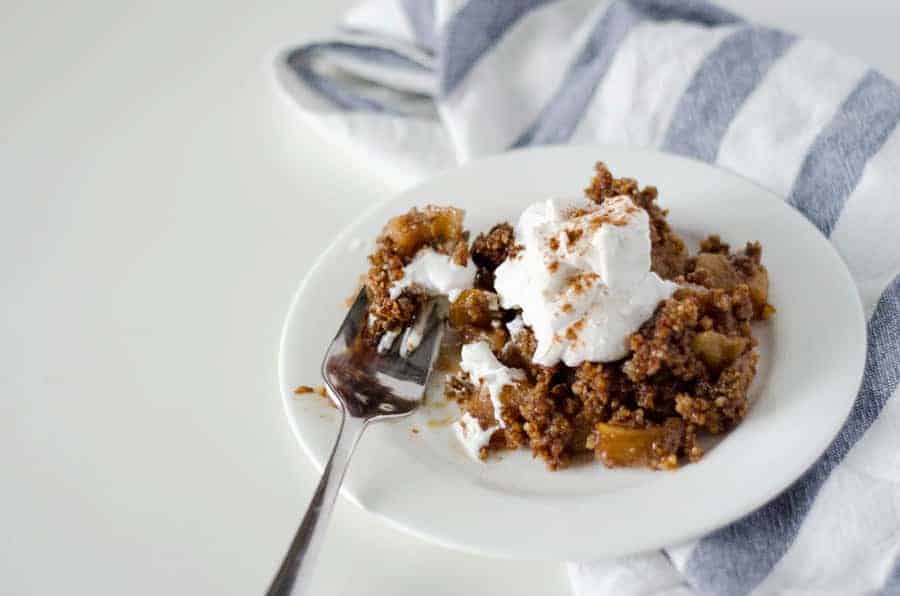 paleo apple crisp on a white plate with a fork and blue and white striped towel