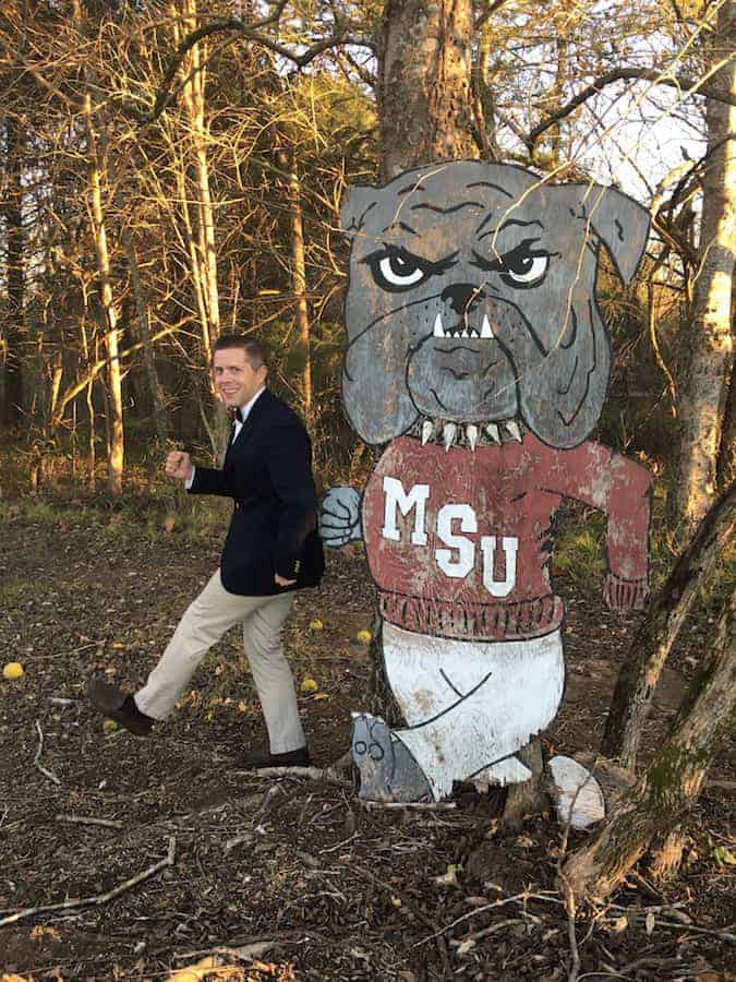 Man in suit standing with MSU bulldog cutout in woods