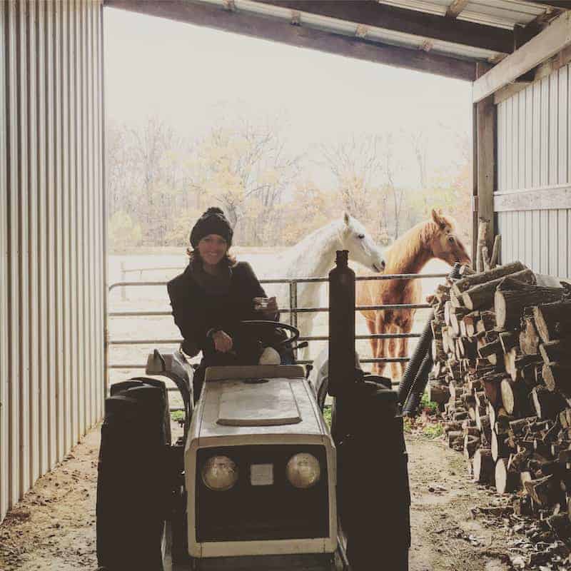 Woman on tractor with horses in background 