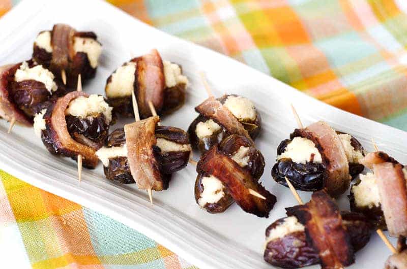 Overhead view of a long white plate holding bacon wrapped dates on top of a plaid napkin