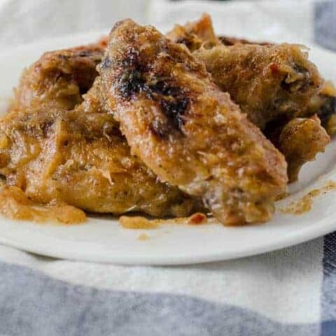 white plate with pile of sticky chicken wings on top of a white and blue dish towel