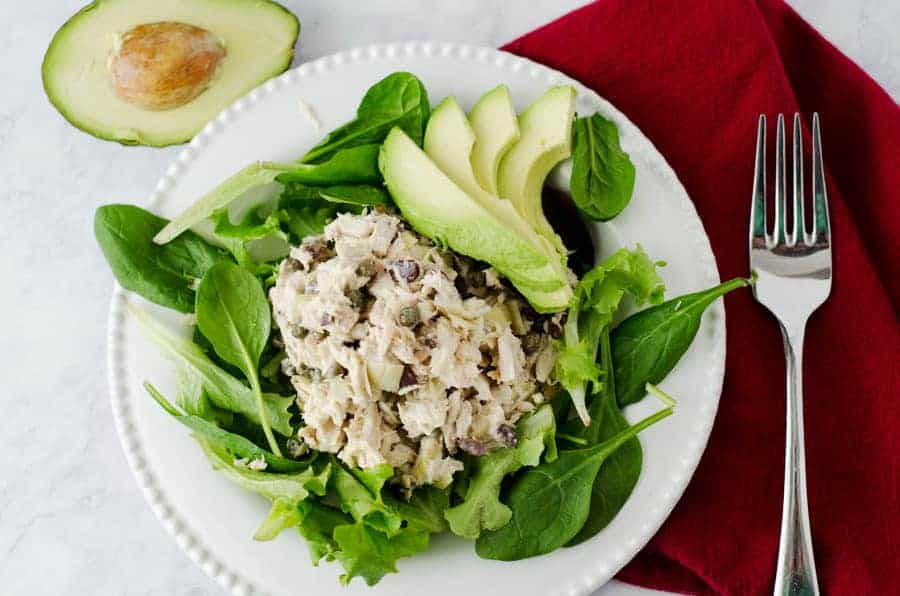 Overhead view of mediterranean tuna salad resting on a bed of greens with a red napkin and fork in the background 