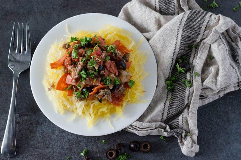 Overhead view of a white plate on a dark background with spaghetti squash topped with a paleo pepperoni pizza sauce