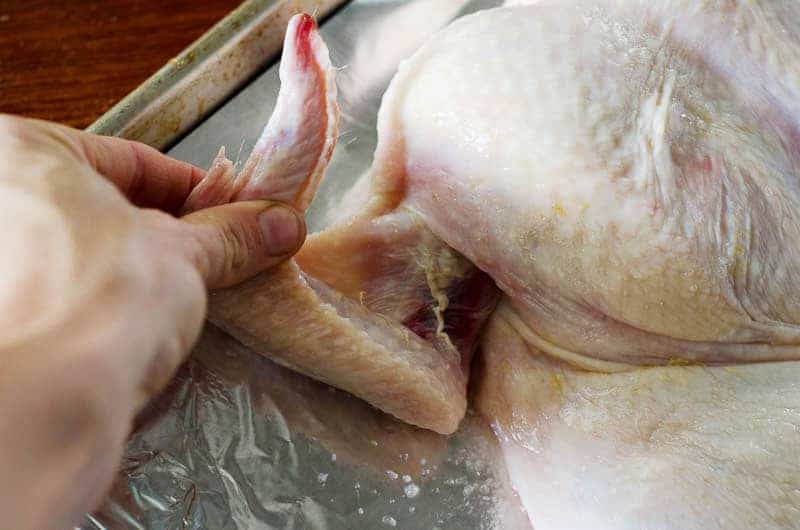 Person's hand holding a chicken wing on a baking sheet