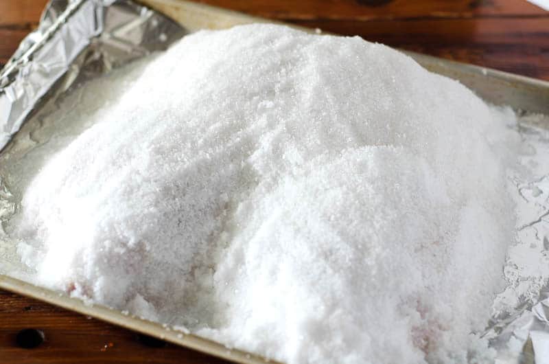 Side view of a chicken on a baking sheet covered in a salt crust