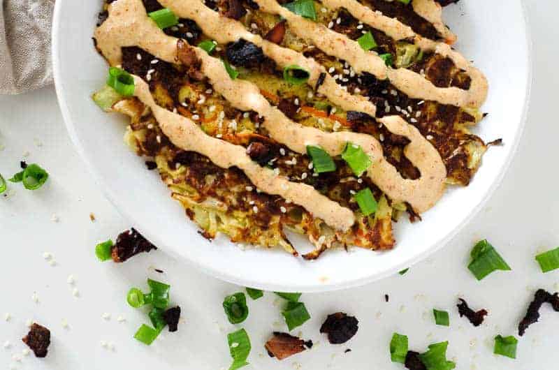 Overhead view of Gluten Free Okonomiyaki (Japanese Cabbage Pancake)  on a white plate drizzled with sauce