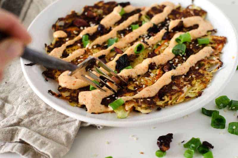 side view of hand holding fork cutting into an Okonomiyaki (Japanese Cabbage Pancake)