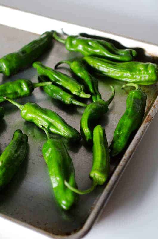 Roasting pan with raw bright green shishito peppers on it