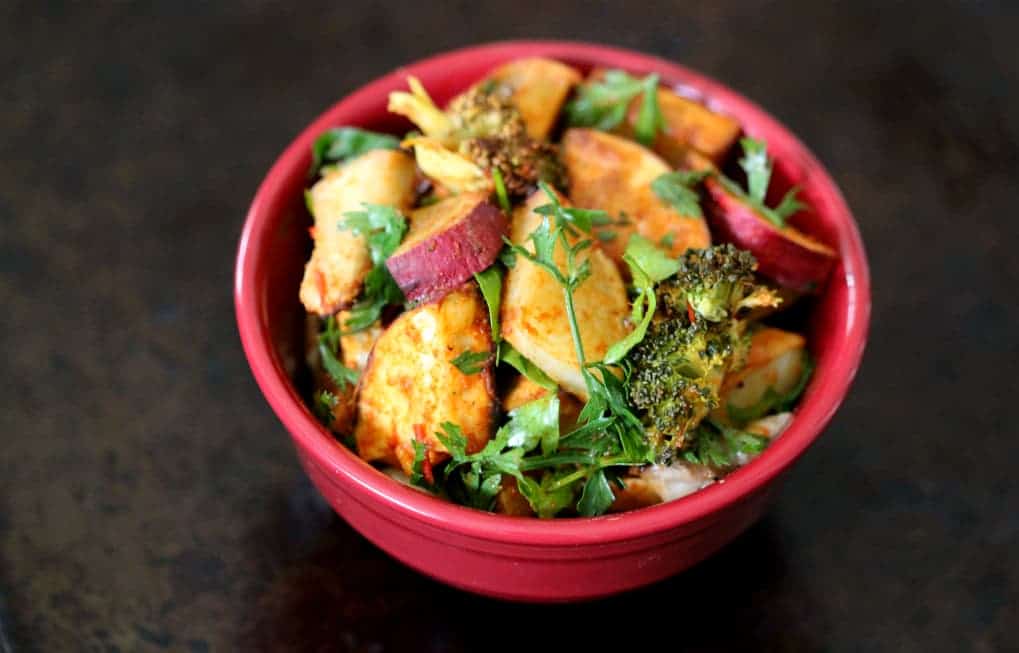 side-overhead view of a red bowl on a dark background with potato salad and fresh herbs