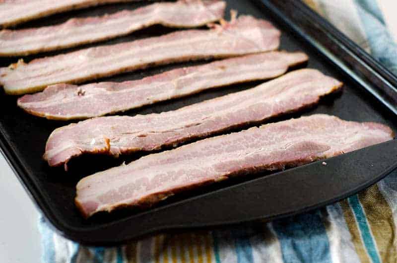 raw bacon slices laid out on baking sheet