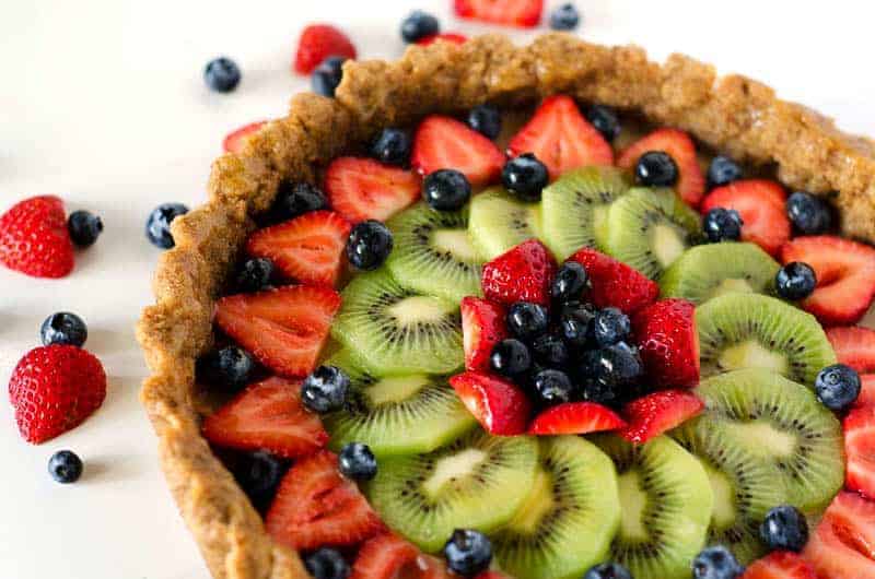 Side view of a mixed fruit tart surrounded by berries