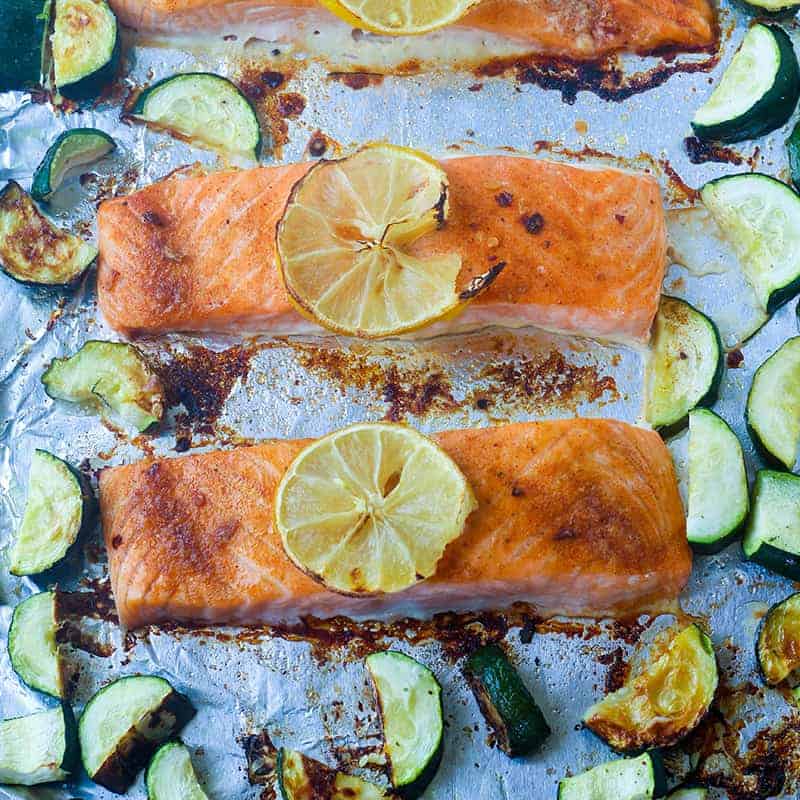 overhead view of salmon filets topped with lemon on a foil lined pan