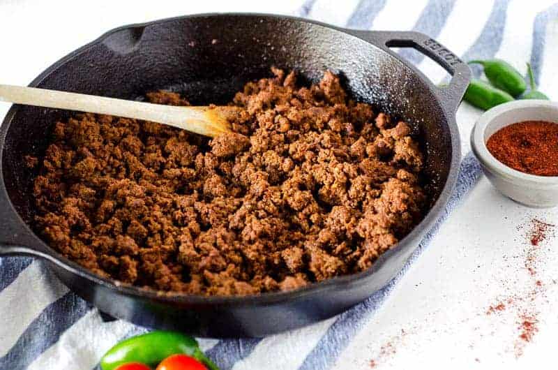 Side view of cast iron skillet filled with Whole30 taco meat surrounded by peppers and spices