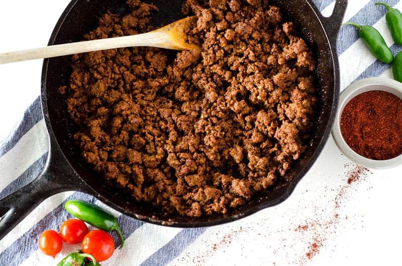 Overhead view of taco meat in a cast iron skillet on a blue and white striped dish towel