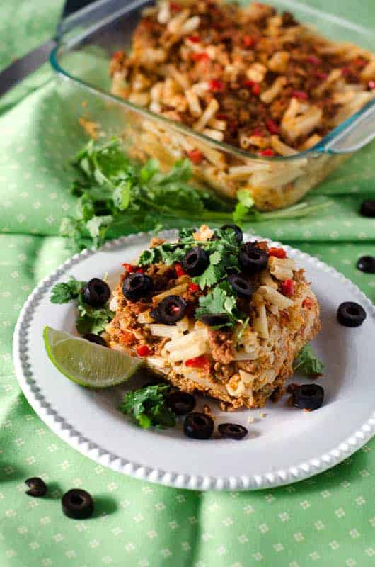 Side view of chicken taco casserole served on a white plate with the casserole dish in the background