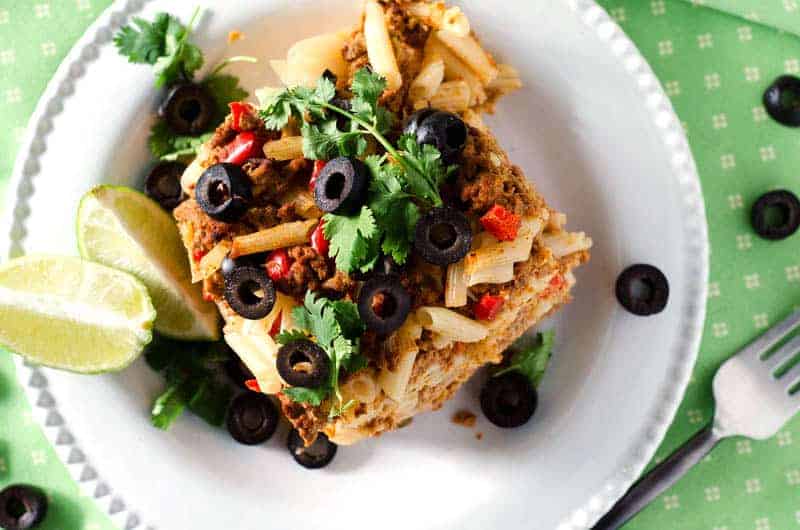 Close up overhead view of chicken taco casserole served on a white plate on a green tablecloth with a fork next to it