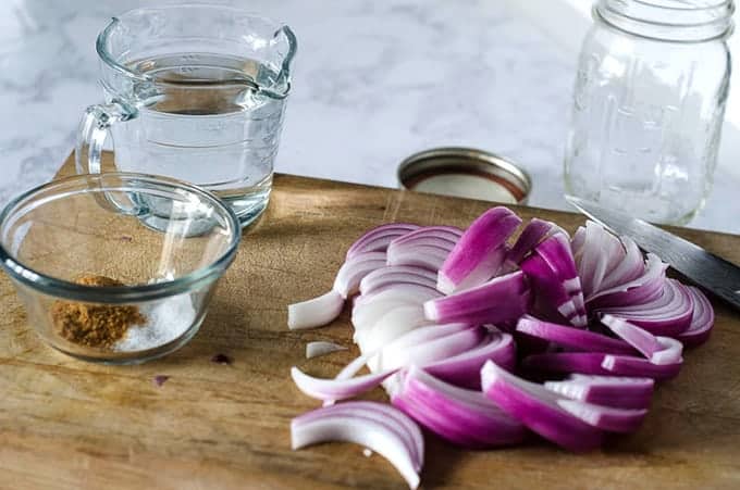 Side view of a cutting board with sliced red onion and pickling ingredients