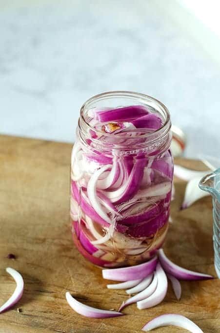 Side view of a mason jar full of red onion slices and vinegar