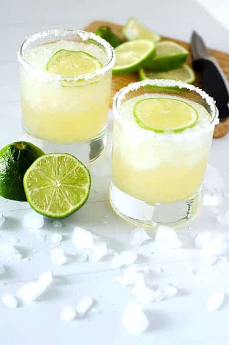 two glasses of paleo margaritas on the rocks surrounded by limes and ice