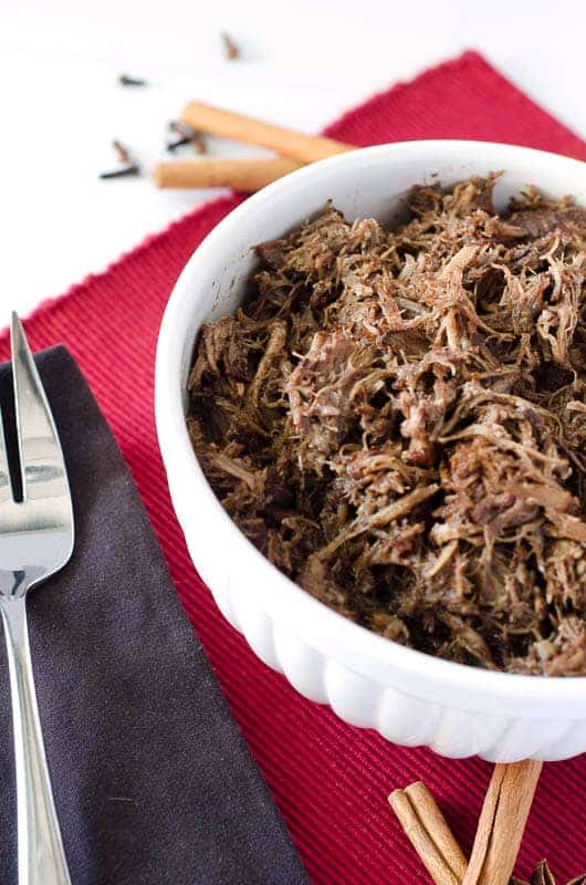 white bowl of pulled pork on a red placemat with large silver serving fork