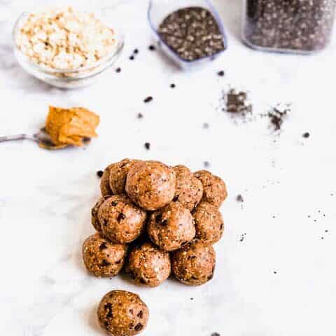 Pile of energy ball snacks on counter surrounded by oats, peanut butter and chia seeds