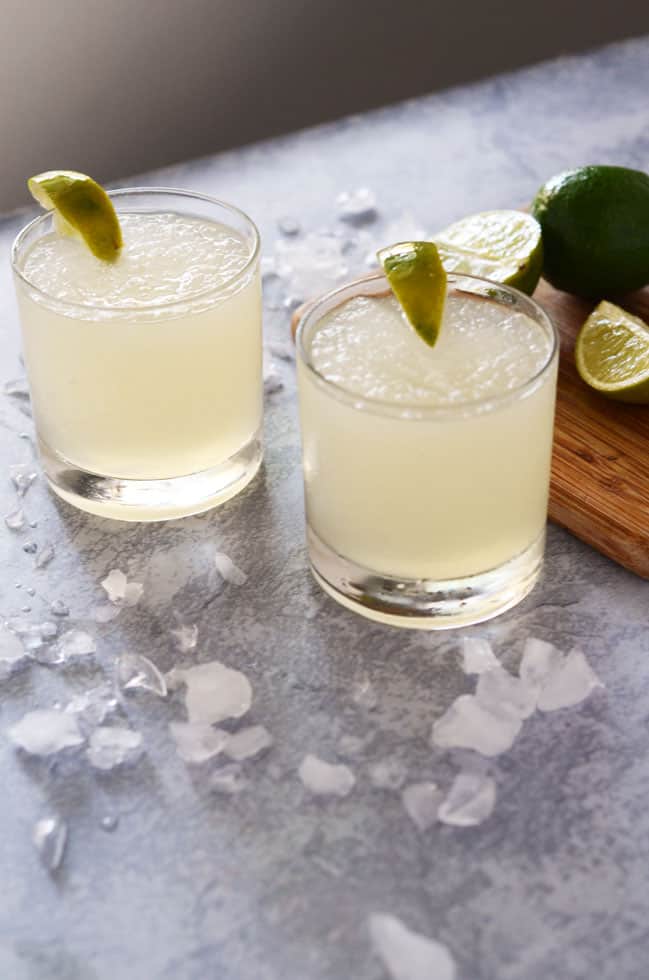 two glasses of frozen limeade surrounded by ice cubes