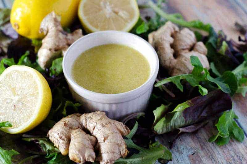 bowl of ginger dressing surrounded by lettuce, ginger, and lemons