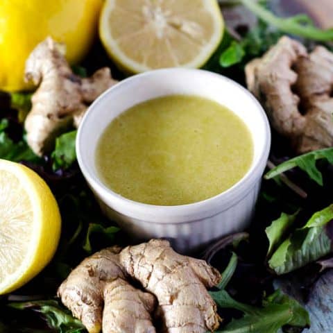 bowl of ginger dressing surrounded by lemons, ginger, and lettuce leaves