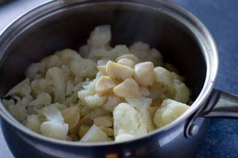 stainless steel pot with steamed cauliflower florets and closed of roasted garlic