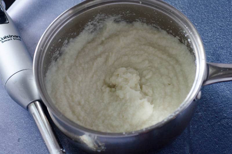 stainless steel pot full of cauliflower mashed potatoes with immersion blender next to it