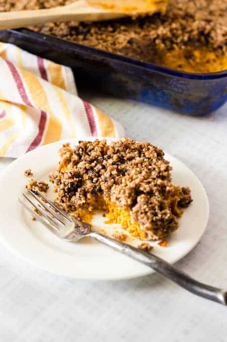 white plate with serving of sweet potato casserole and fork on it with casserole dish in the background