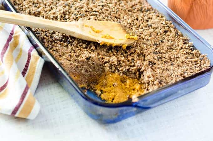 blue casserole dish on counter full of sweet potato casserole with a serving scooped out and wooden spoon on top