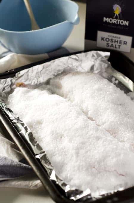 Baking sheet lined with foil with two fish covered in a salt crust on it before baking