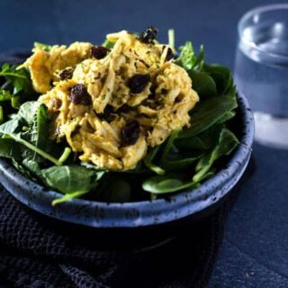 dark bowl of mixed greens salad topped with a scoop of curry cashew chicken salad