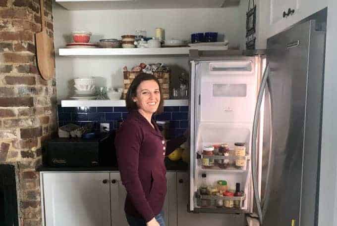 Woman standing at refrigerator holding door open and smiling