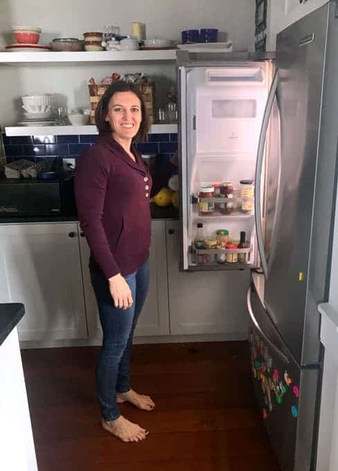 woman standing in front of fridge in bare feet holding door open and smiling