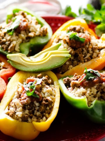 plate of bell peppers cut and open faced stuffed with taco meat and topped with cilantro and avocado