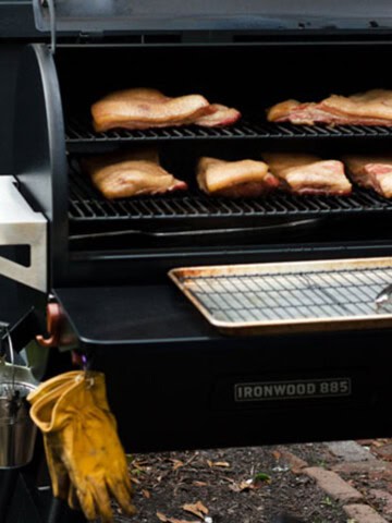 open traeger grill with slabs of pork belly smoking on it and yellow gloves hanging in the foreground