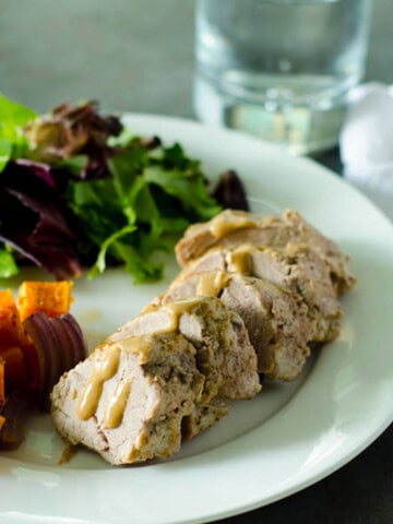 pork tenderloin sliced with a mustard glaze and on a plate with sweet potatoes and salad greens